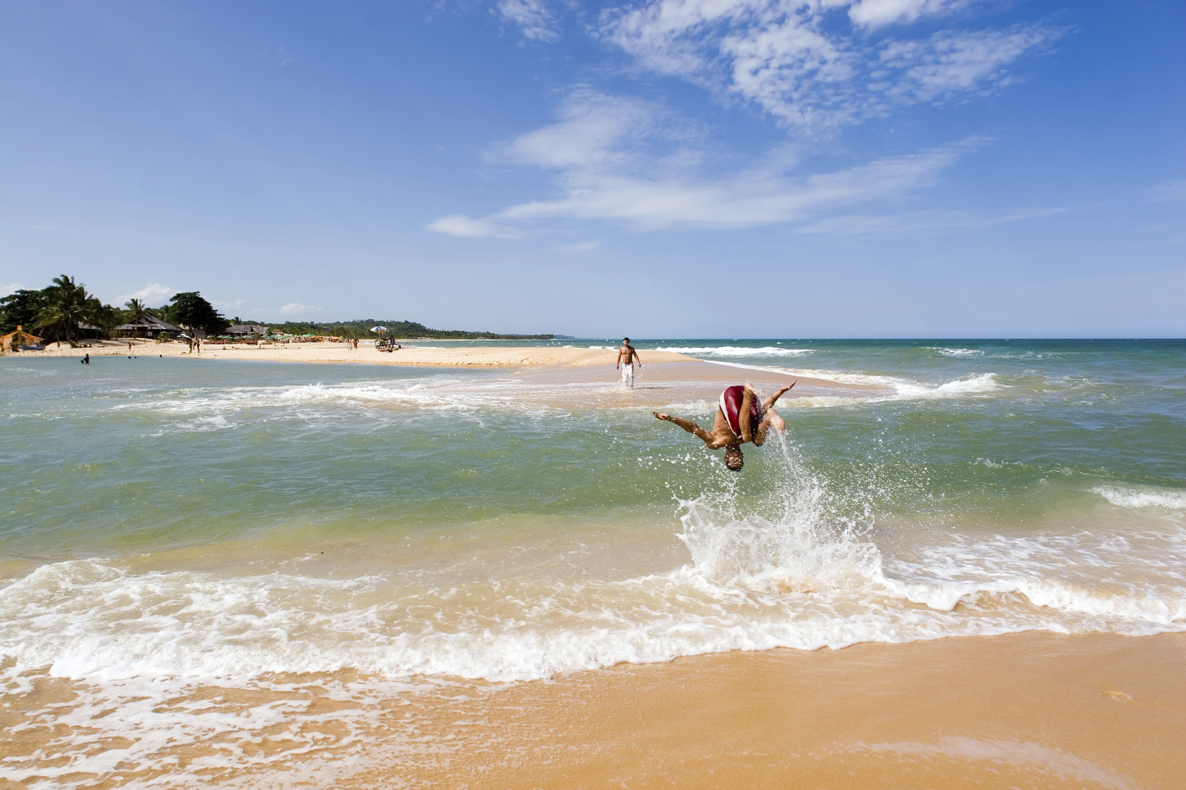 healthy young man in action having fun, playing and somersalting on a acrobat fashion, upside down, on the waters of a green river that meets the sea in a beautiful and sunny tropical beach healthy young man in action having fun, playing and somersalting on a acrobat fashion, upside down, on the waters of a green river that meets the sea in a beautiful and sunny tropical beach